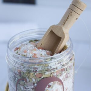Close-up of natural bath salt in a plastic container with a wooden scoop, ideal for relaxation and skincare.