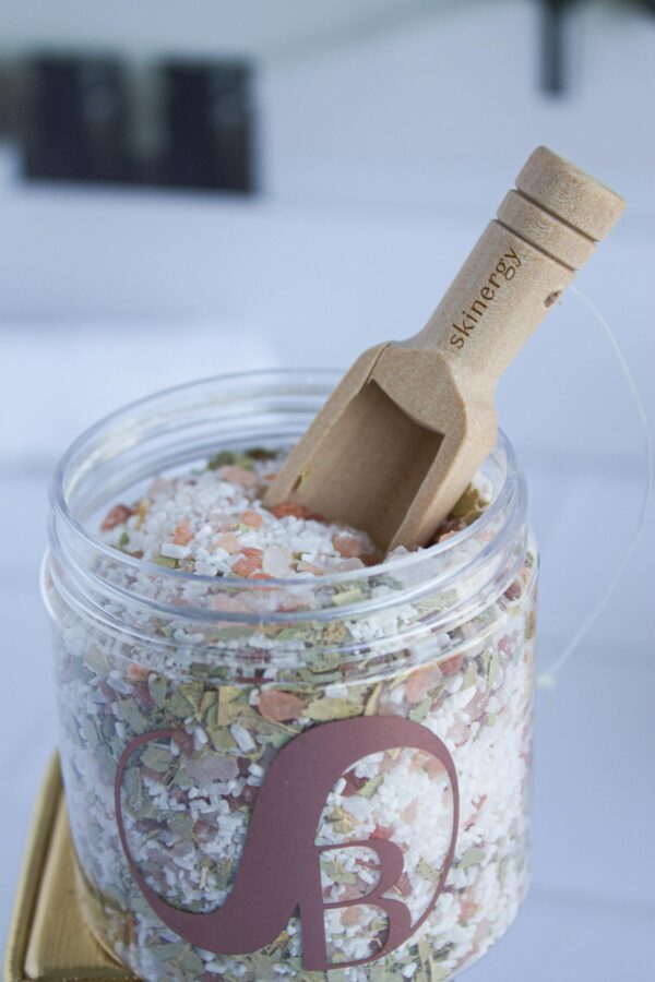 Close-up of natural bath salt in a plastic container with a wooden scoop, ideal for relaxation and skincare.